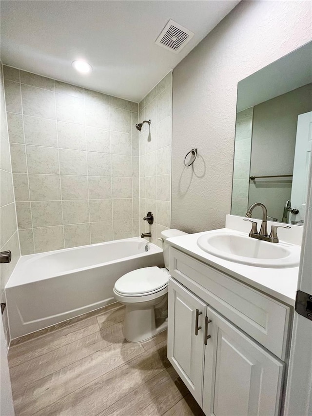 full bathroom featuring toilet, wood finished floors, vanity, visible vents, and shower / washtub combination