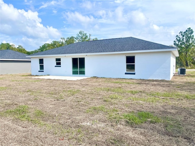 back of house featuring roof with shingles, cooling unit, a lawn, and stucco siding