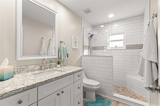 bathroom with vanity, hardwood / wood-style floors, a tile shower, and toilet