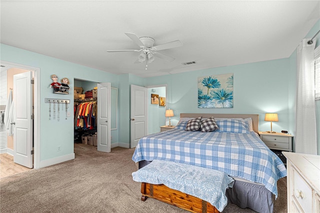 bedroom with connected bathroom, a closet, a walk in closet, light colored carpet, and ceiling fan