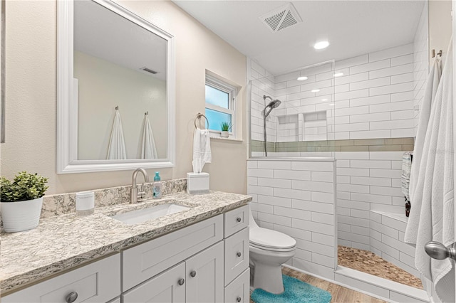 bathroom featuring vanity, a tile shower, wood-type flooring, and toilet