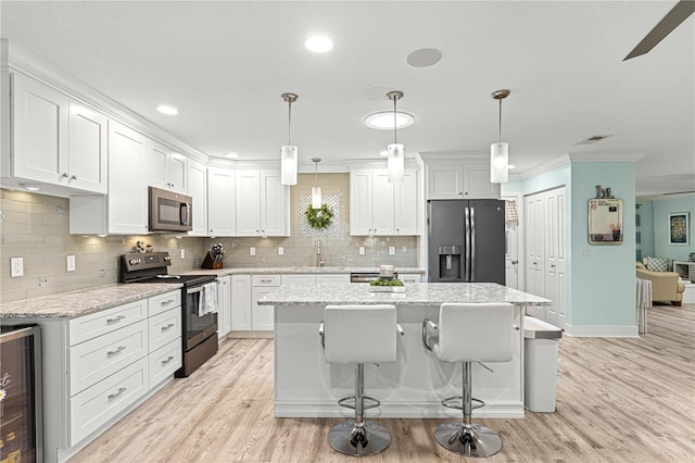 kitchen featuring white cabinets, stainless steel appliances, hanging light fixtures, and light wood-type flooring