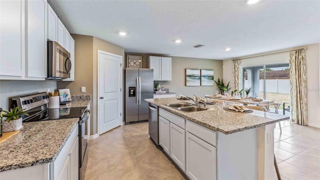 kitchen with light stone counters, an island with sink, white cabinetry, sink, and stainless steel appliances