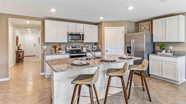 kitchen with a center island with sink, white cabinetry, stainless steel appliances, and light stone countertops