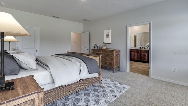 bedroom with a textured ceiling, light carpet, and ensuite bathroom