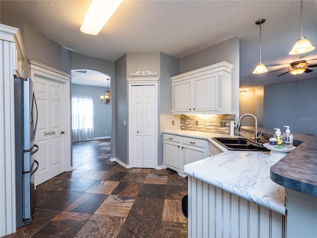 kitchen with sink, stainless steel fridge, white cabinetry, hanging light fixtures, and decorative backsplash