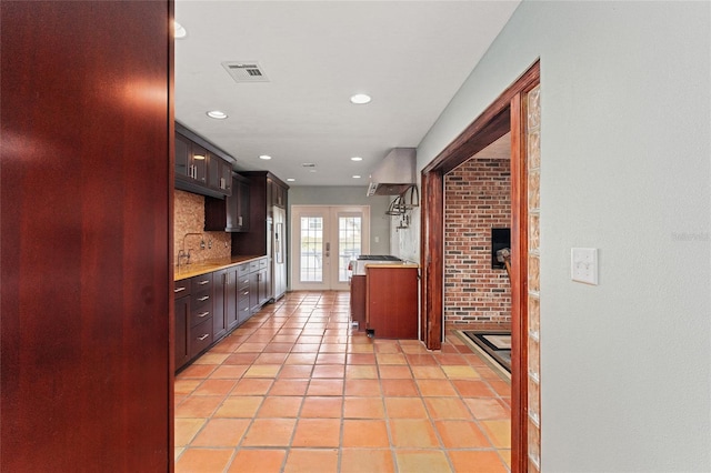 kitchen featuring tasteful backsplash, high end refrigerator, light tile patterned floors, french doors, and brick wall