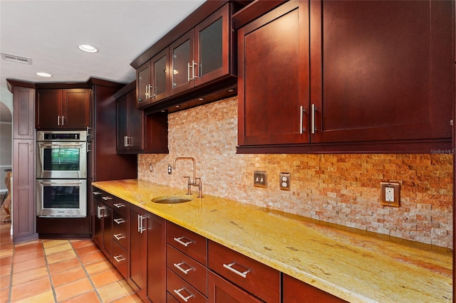 kitchen featuring light stone countertops, light tile patterned flooring, sink, double oven, and decorative backsplash