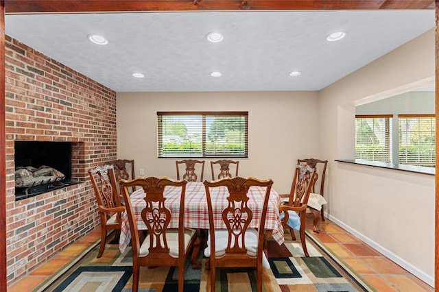 dining area featuring brick wall, light tile patterned flooring, a fireplace, and a healthy amount of sunlight