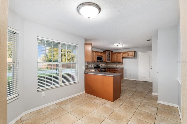 kitchen featuring appliances with stainless steel finishes, sink, kitchen peninsula, decorative backsplash, and light tile patterned floors