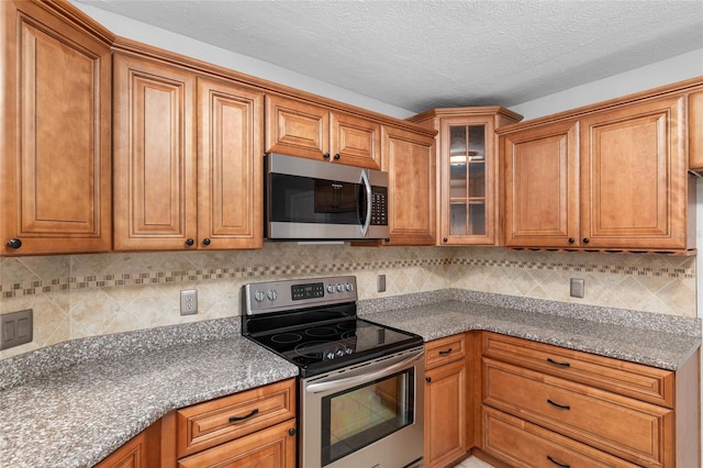 kitchen with light stone countertops, appliances with stainless steel finishes, a textured ceiling, and decorative backsplash