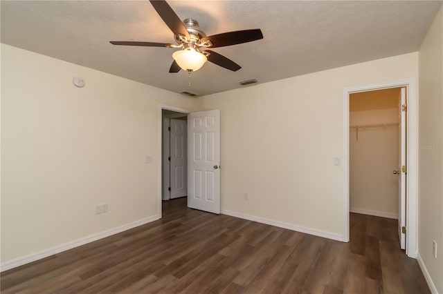 unfurnished bedroom featuring ceiling fan, dark hardwood / wood-style flooring, a textured ceiling, a spacious closet, and a closet