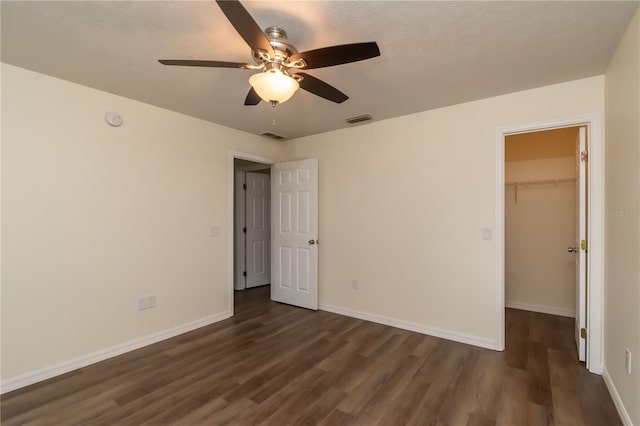 unfurnished bedroom featuring dark hardwood / wood-style floors, a spacious closet, ceiling fan, a textured ceiling, and a closet