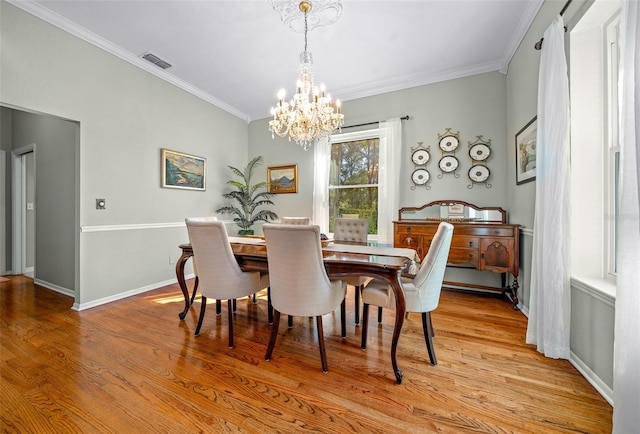 dining space with light hardwood / wood-style floors, crown molding, and a notable chandelier