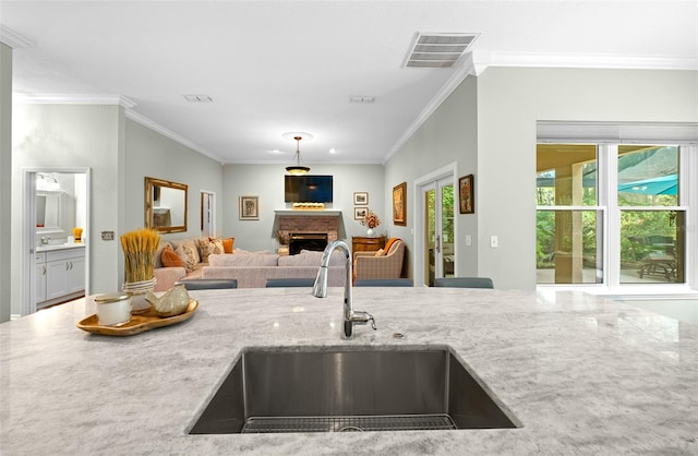 kitchen featuring light stone countertops, a brick fireplace, ornamental molding, pendant lighting, and sink