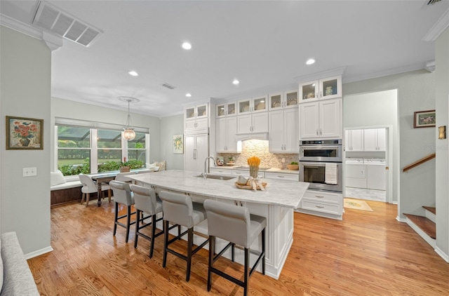 kitchen with stainless steel double oven, washer and clothes dryer, sink, light wood-type flooring, and white cabinetry