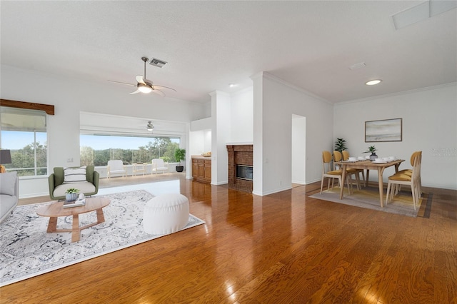 living room with ceiling fan, dark hardwood / wood-style flooring, ornamental molding, and a fireplace