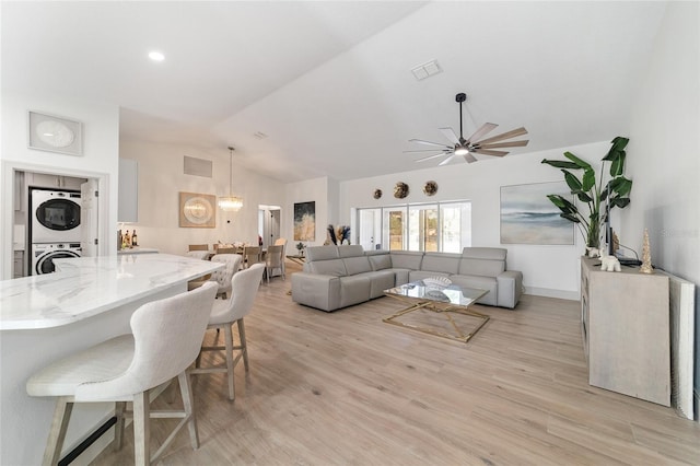 living room featuring lofted ceiling, stacked washer / dryer, ceiling fan with notable chandelier, and light wood-type flooring