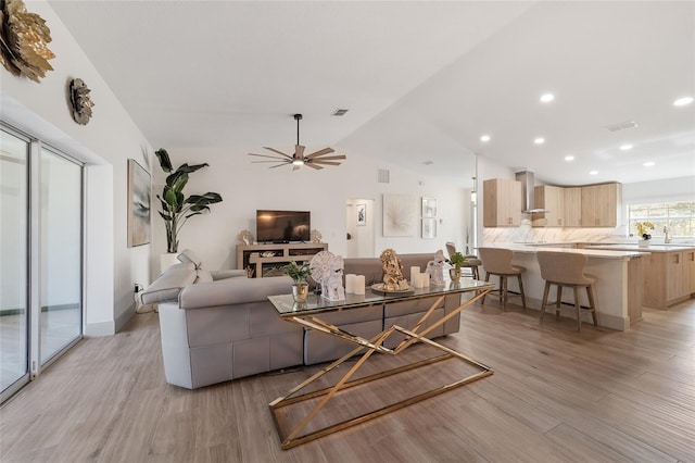 living room with vaulted ceiling, light hardwood / wood-style flooring, a fireplace, and ceiling fan