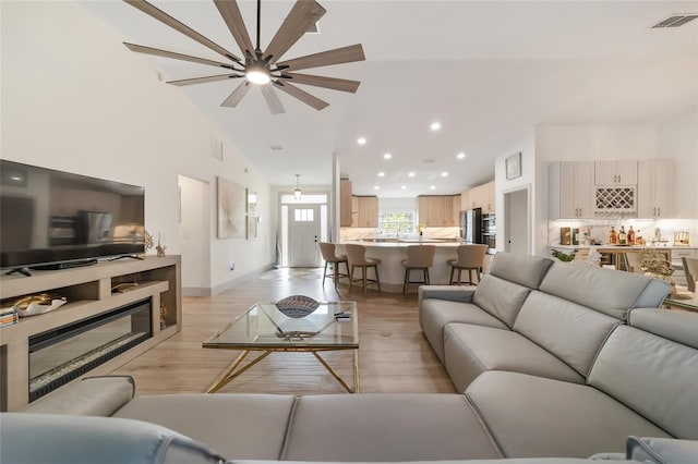 living room with light hardwood / wood-style flooring, high vaulted ceiling, and ceiling fan