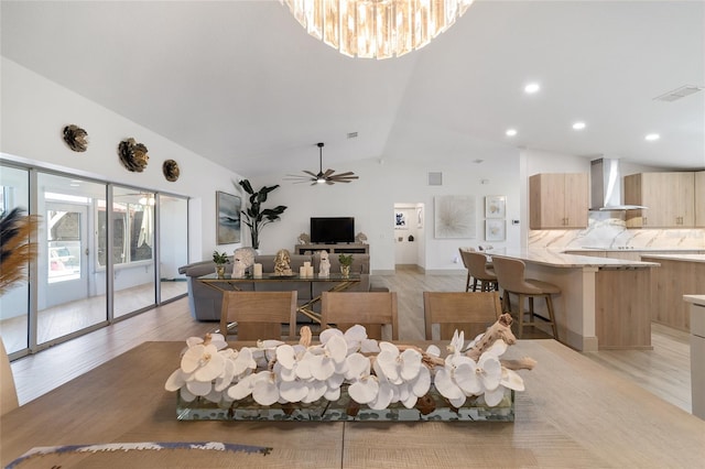 living room featuring light hardwood / wood-style floors, ceiling fan with notable chandelier, and vaulted ceiling