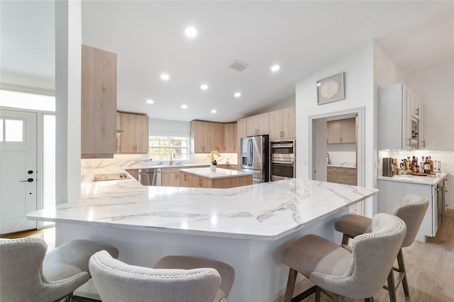 kitchen featuring appliances with stainless steel finishes, light wood-type flooring, backsplash, kitchen peninsula, and a breakfast bar