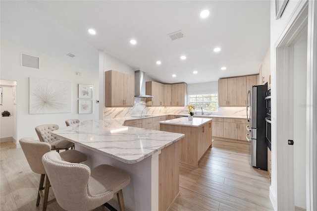 kitchen featuring wall chimney range hood, lofted ceiling, a kitchen island, a breakfast bar, and light hardwood / wood-style flooring