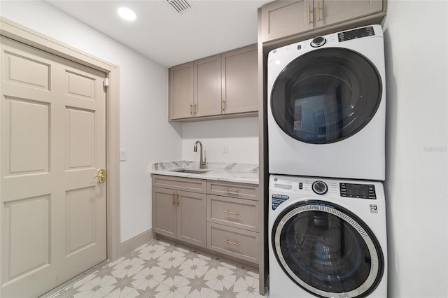 clothes washing area featuring sink, stacked washer and dryer, and cabinets