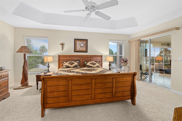 carpeted bedroom with access to outside, a tray ceiling, and ceiling fan