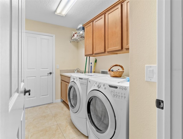 clothes washing area featuring washer and dryer, light tile patterned floors, sink, a textured ceiling, and cabinets