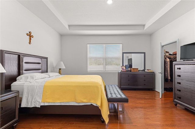 bedroom featuring dark hardwood / wood-style flooring, a walk in closet, a tray ceiling, and a closet