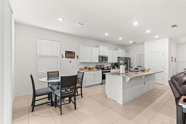 kitchen featuring light stone countertops, a kitchen breakfast bar, stainless steel appliances, white cabinetry, and an island with sink