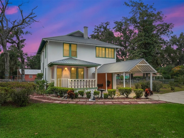 back house at dusk with a porch and a lawn