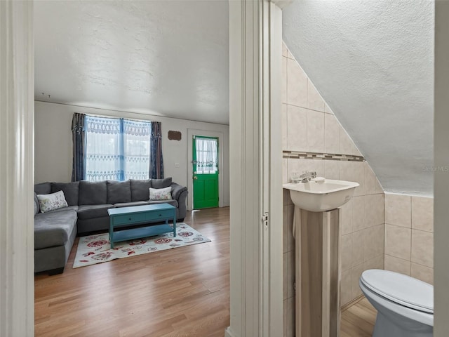 living room featuring sink, a textured ceiling, light hardwood / wood-style floors, tile walls, and vaulted ceiling