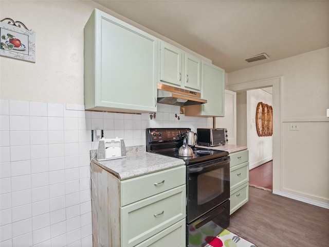 712 SW 10th Ave, Ocala, FL 34471 - kitchen featuring black / electric stove, under cabinet range hood, wood finished floors, and tasteful backsplash