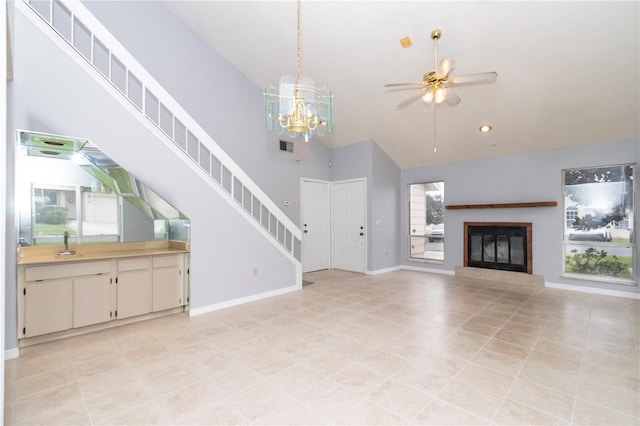 unfurnished living room featuring light tile patterned floors, a high ceiling, ceiling fan with notable chandelier, and plenty of natural light