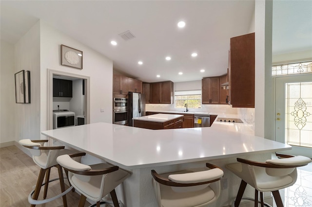 kitchen featuring kitchen peninsula, appliances with stainless steel finishes, a breakfast bar, light hardwood / wood-style floors, and sink