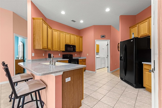 kitchen with kitchen peninsula, a breakfast bar, washer and dryer, black appliances, and sink