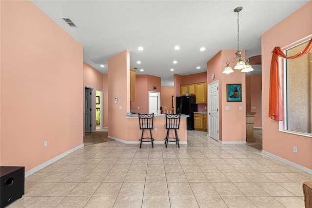 kitchen featuring kitchen peninsula, hanging light fixtures, light tile patterned floors, a kitchen bar, and black refrigerator