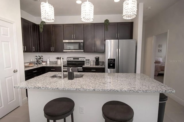 kitchen with a kitchen island with sink, a kitchen bar, pendant lighting, light tile patterned floors, and appliances with stainless steel finishes