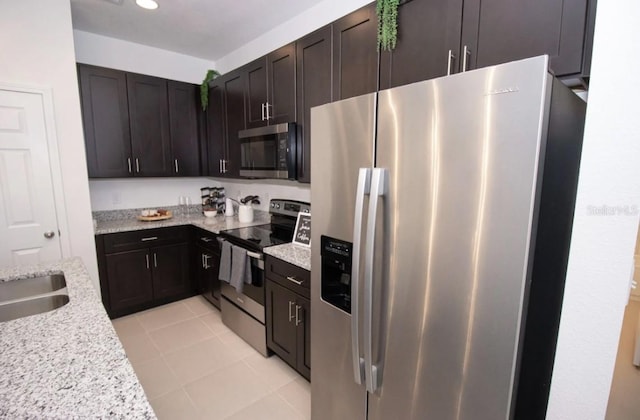 kitchen featuring light stone countertops, stainless steel appliances, and dark brown cabinets