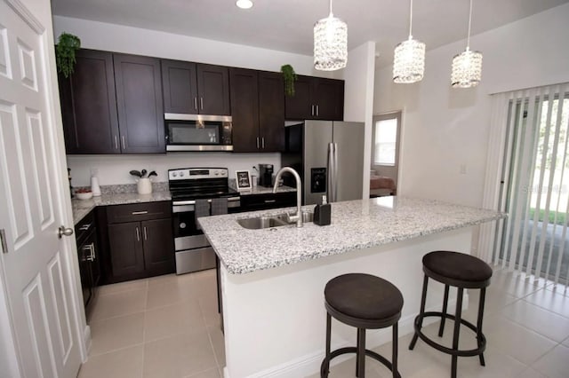 kitchen featuring hanging light fixtures, appliances with stainless steel finishes, a breakfast bar, a kitchen island with sink, and sink