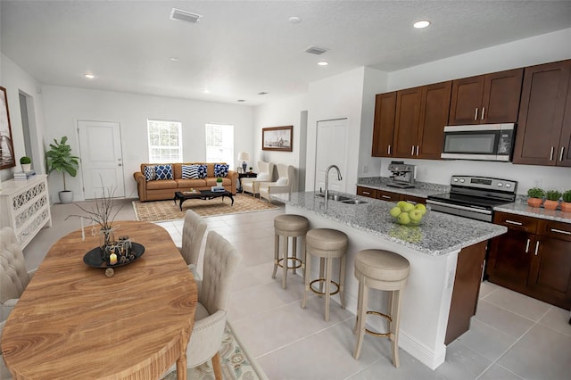 kitchen featuring a breakfast bar area, appliances with stainless steel finishes, light tile patterned floors, an island with sink, and sink