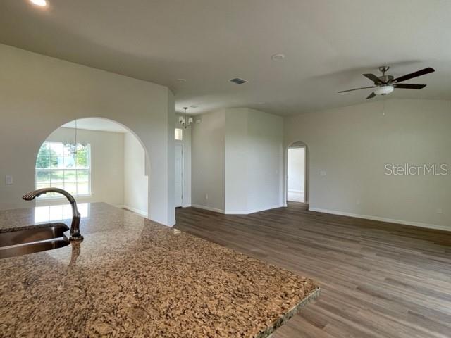 kitchen with hardwood / wood-style flooring, sink, light stone countertops, and ceiling fan with notable chandelier