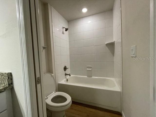 bathroom with tiled shower / bath, hardwood / wood-style flooring, and toilet