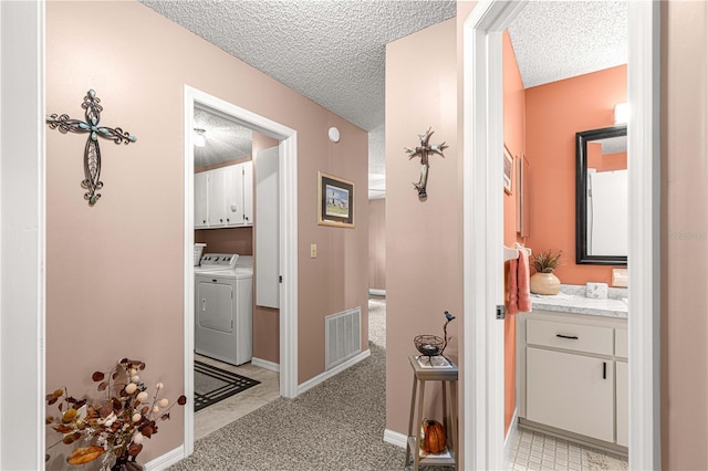 hallway featuring independent washer and dryer, a textured ceiling, and light colored carpet