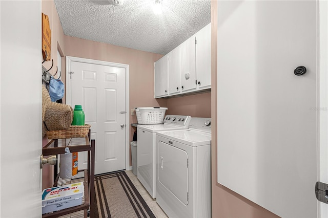 laundry area with washer and dryer, a textured ceiling, and cabinets