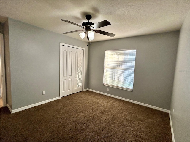 unfurnished bedroom with ceiling fan, a closet, a textured ceiling, and dark colored carpet