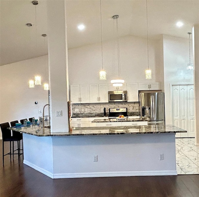 kitchen with dark wood-type flooring, dark stone countertops, pendant lighting, white cabinets, and appliances with stainless steel finishes