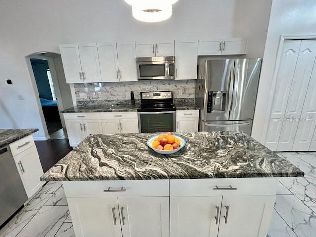 kitchen featuring a kitchen island, white cabinetry, stainless steel appliances, and dark stone counters